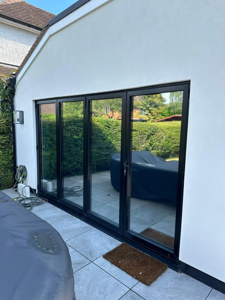 Exterior view of a modern bifold door with sleek black frames, installed with mirrored window film for privacy and heat reduction.